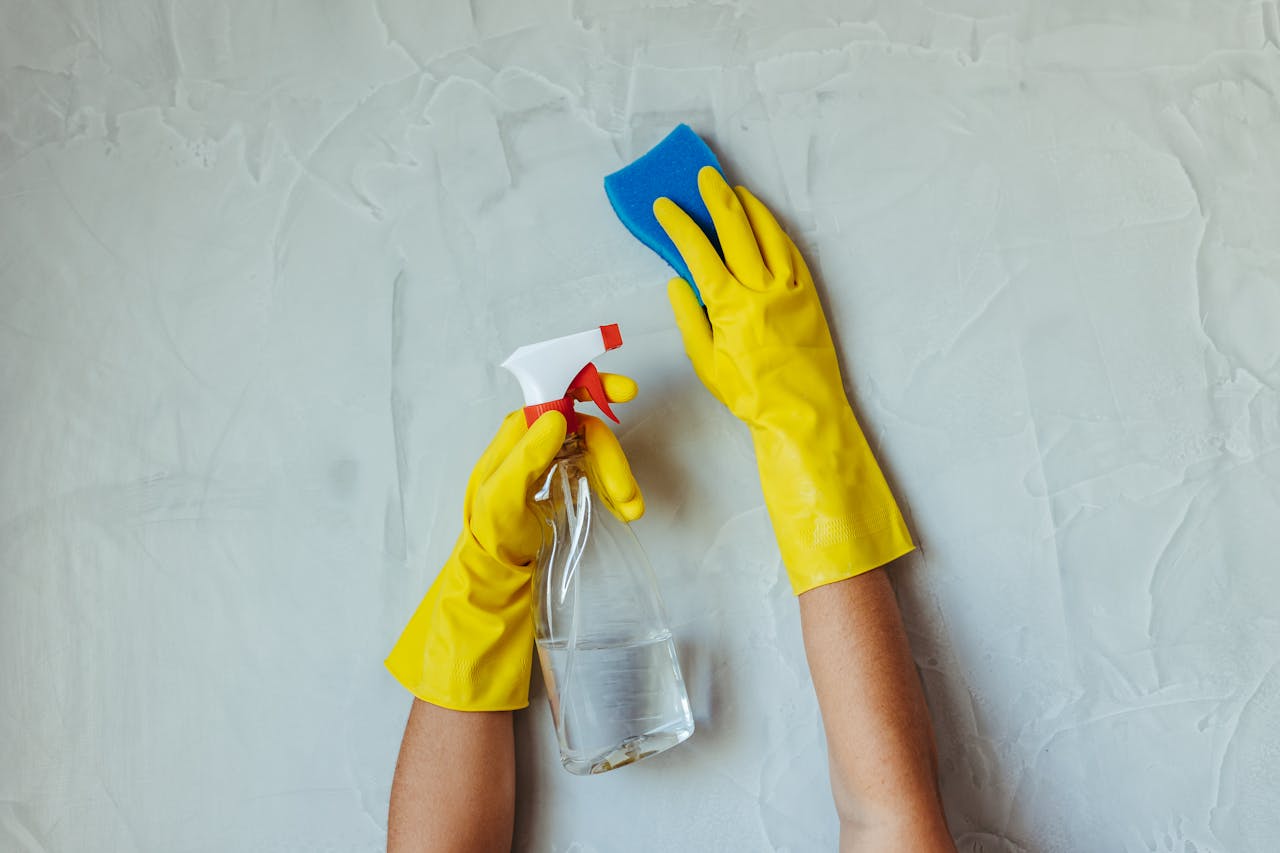 services-01 Close-up of hands in yellow gloves cleaning a wall with a spray bottle and sponge.