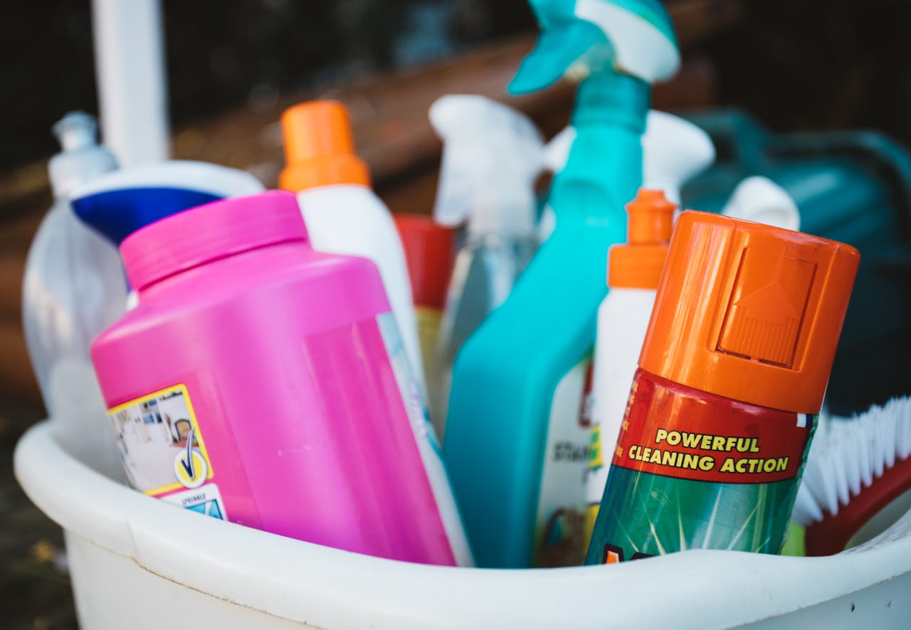 services-02 Close-up of assorted cleaning supplies in a bucket outdoors, showcasing various detergents and sprays.